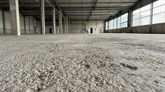 Plancher industriel d'entrepôt montrant surface de béton préparée mécaniquement avec texture d'agrégats exposés et rugosité visible sous éclairage naturel